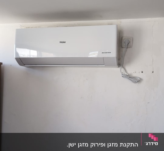 מזגן קיר לבן מותקן על קיר עם שקע חשמל